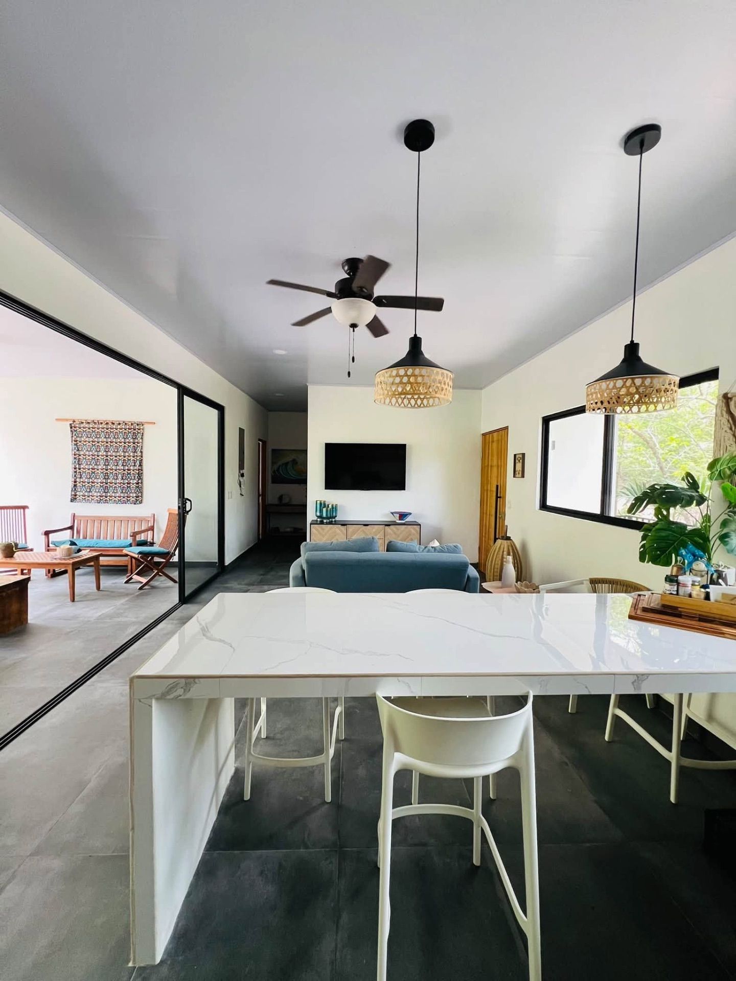 Open-plan living area with marble breakfast bar, blue sofa, wall-mounted TV, ceiling fan and sliding doors to a terrace