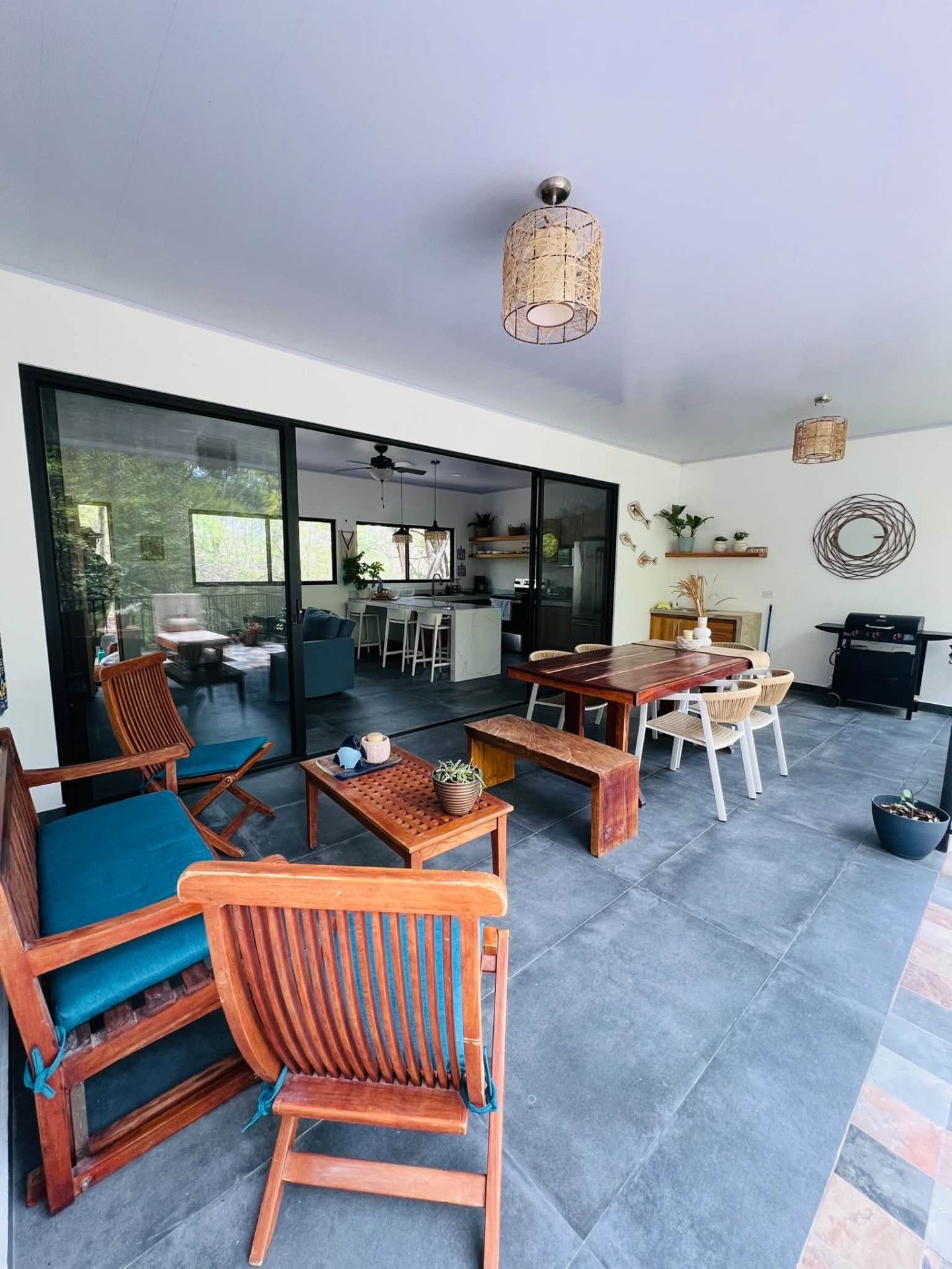 Covered terrace with wooden lounge chairs, dining table for six and a gas grill, opening onto the kitchen