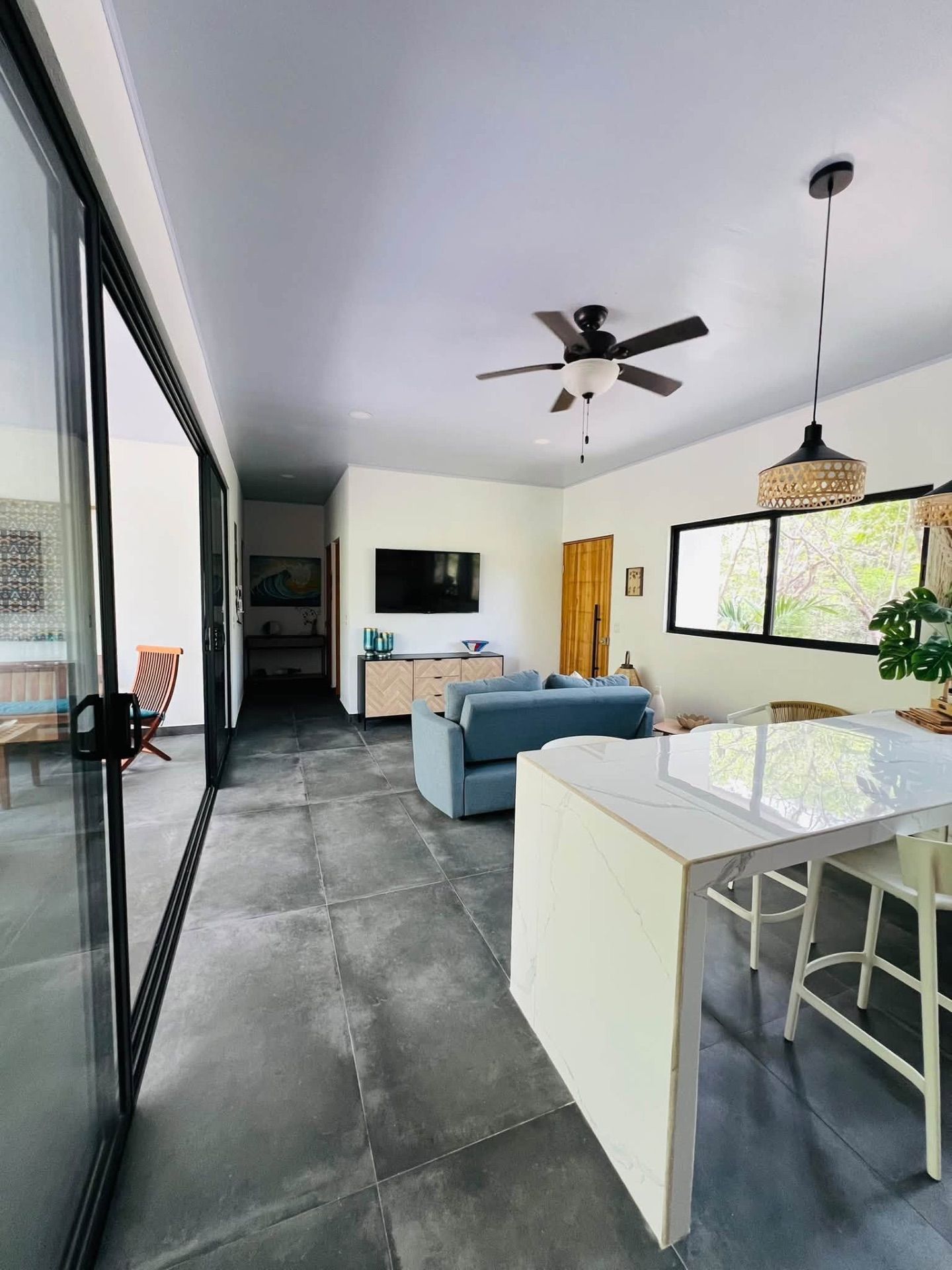 Living area with blue sofa, wall-mounted TV, ceiling fan and marble bar beside glass sliding doors