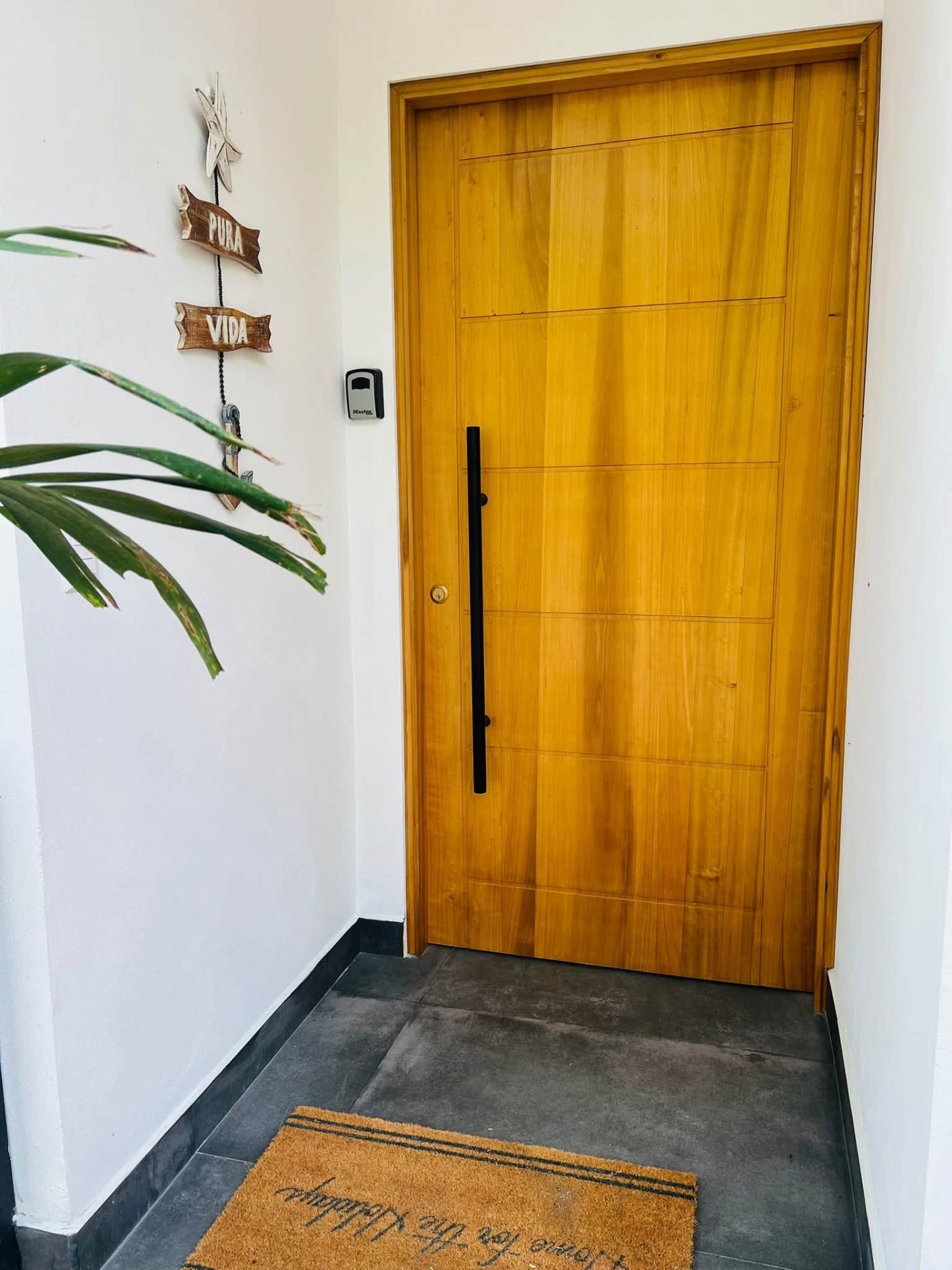 Wooden front door with a key lockbox beside it and a doormat