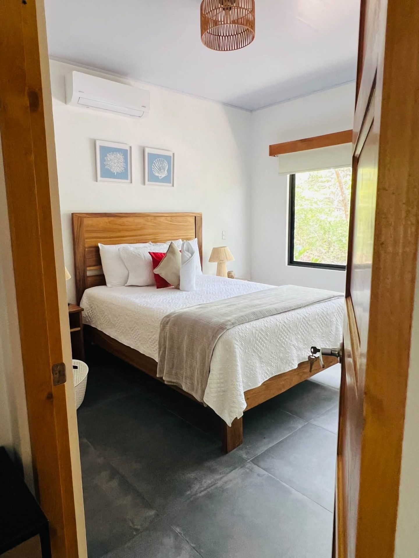 Bedroom with a queen bed, wall-mounted air conditioner and a window facing trees