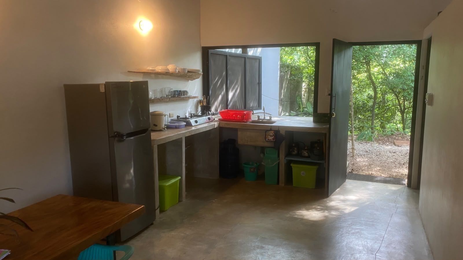 Kitchen with a fridge, two-burner gas stove, sink and open shelves, with a door opening to the garden