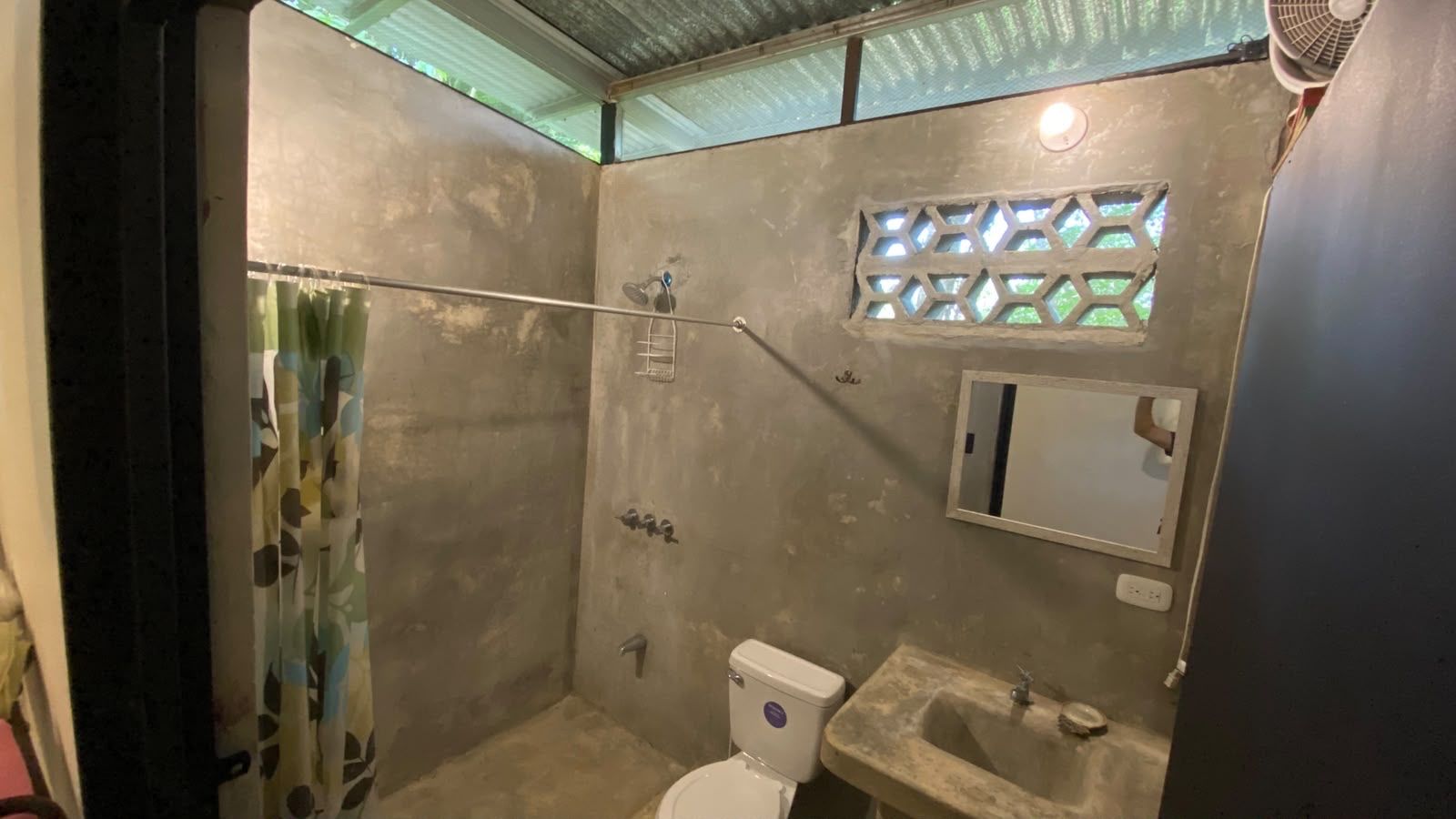 Concrete bathroom with a curtained walk-in shower, toilet, sink and mirror