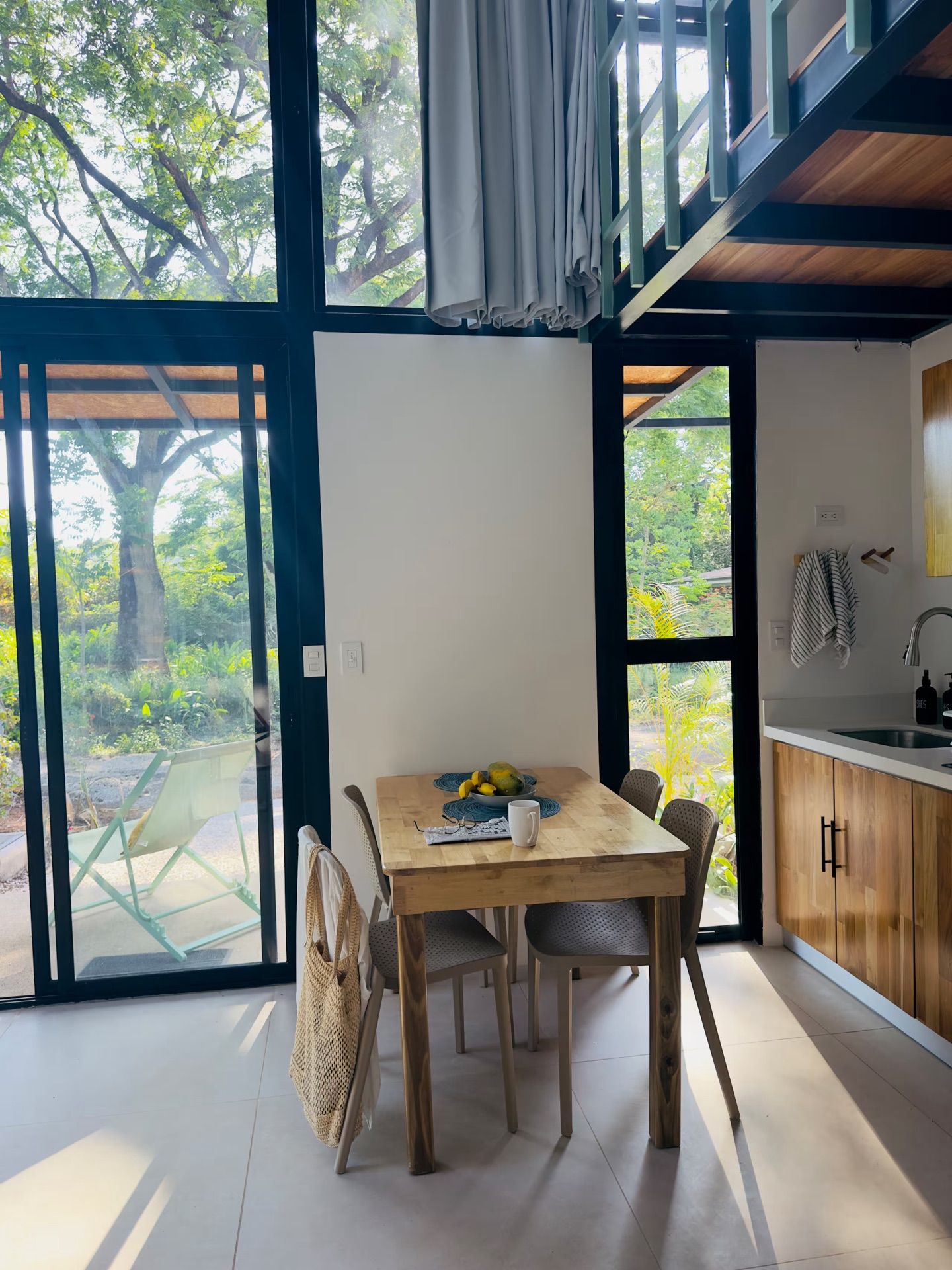 Dining table for four beside glass doors to a patio with a lounge chair, next to the kitchen sink and cabinets