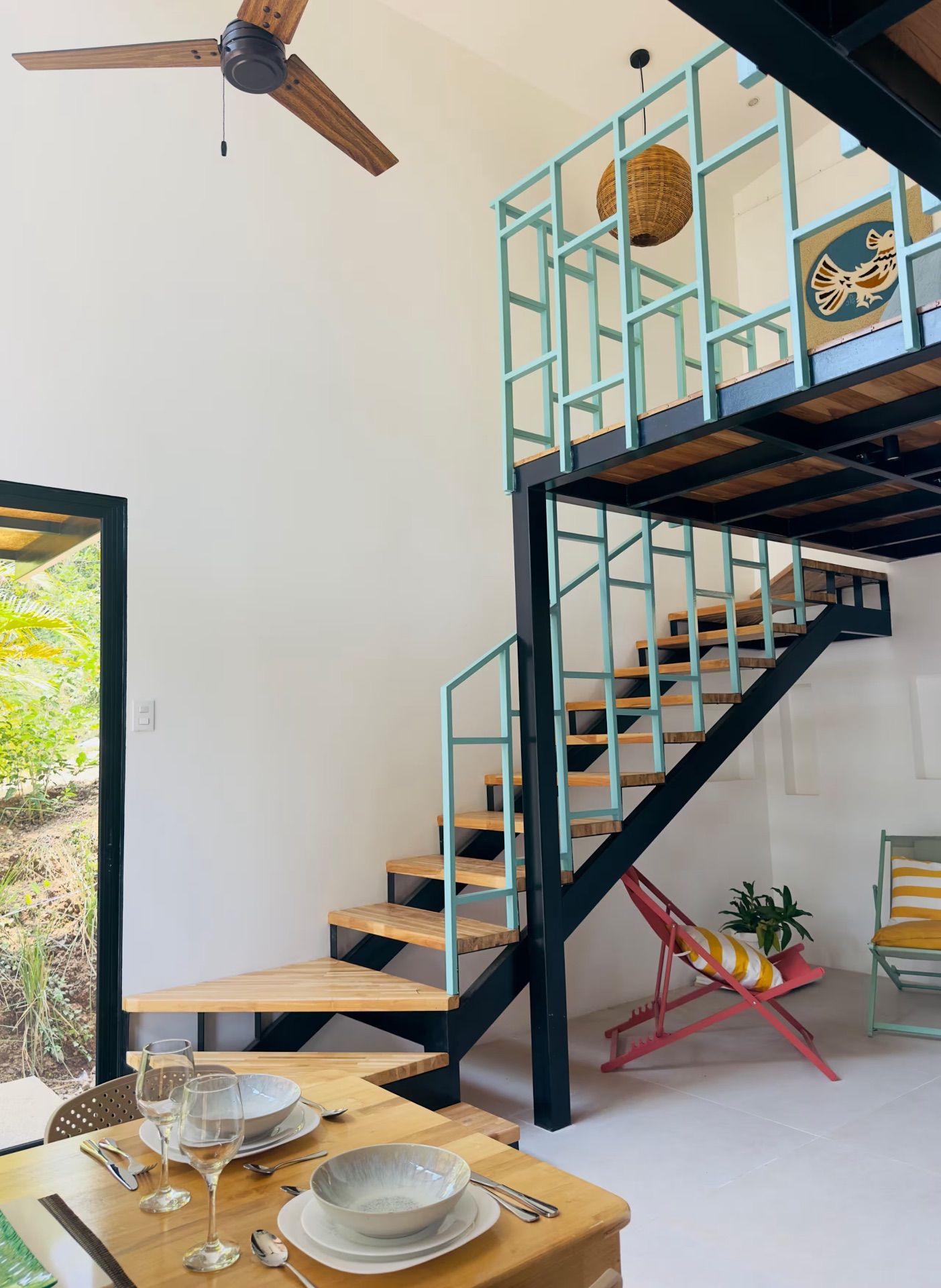 Open living area with a set dining table, ceiling fan and open staircase to a loft, with a door to the garden