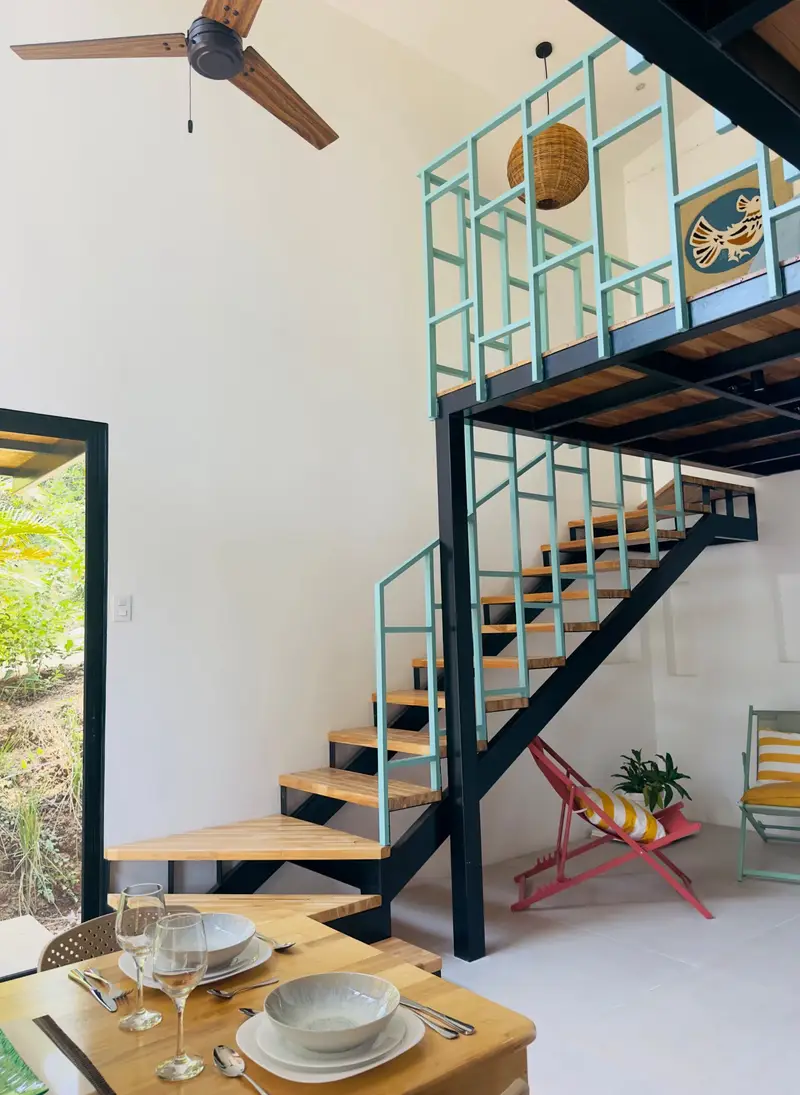 Open living area with a set dining table, ceiling fan and open staircase to a loft, with a door to the garden