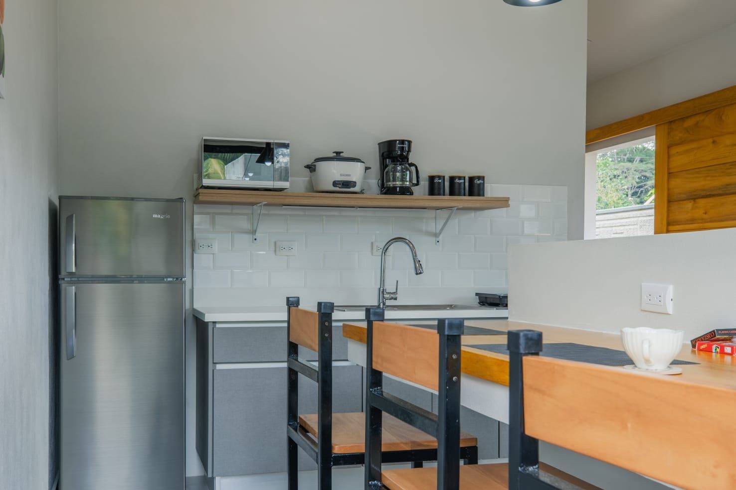 Kitchenette with stainless fridge, sink, microwave, rice cooker and coffee maker beside a breakfast bar with stools