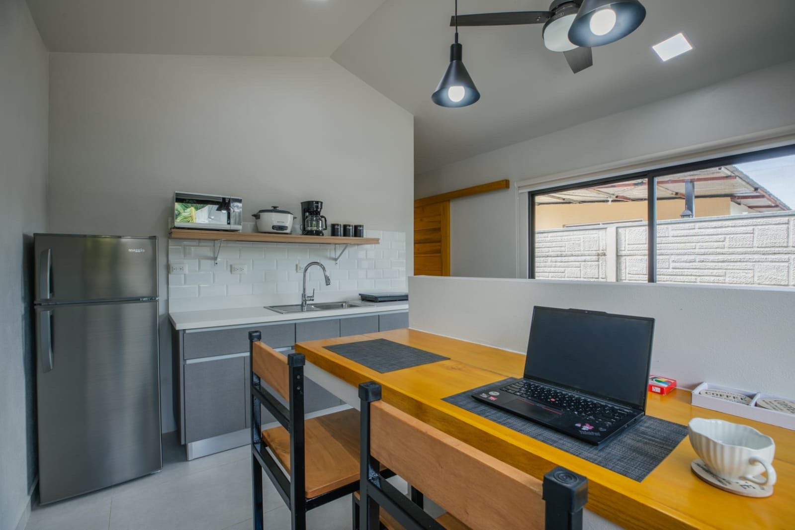 Kitchenette with fridge, microwave and coffee maker beside a wooden counter desk with a laptop and two chairs