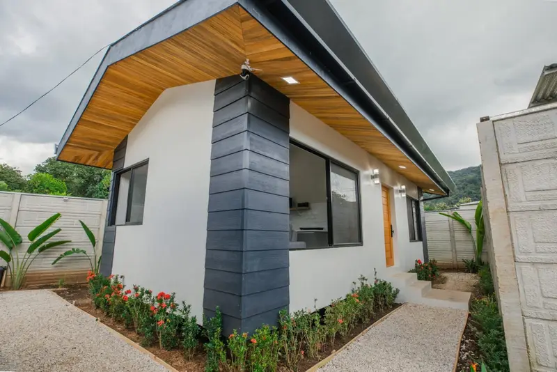Single-storey white house with wood-lined eaves, gravel paths and flowering shrubs inside a walled yard