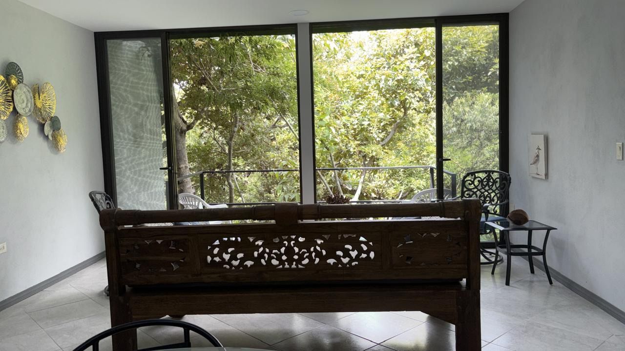 Living area with a carved wooden daybed facing glass doors that open to a balcony among trees